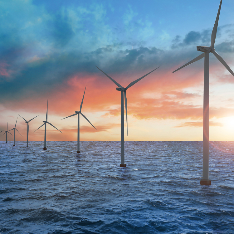 Havvindmøllepark med vindmøller mod en dramatisk orange og blå solnedgang.